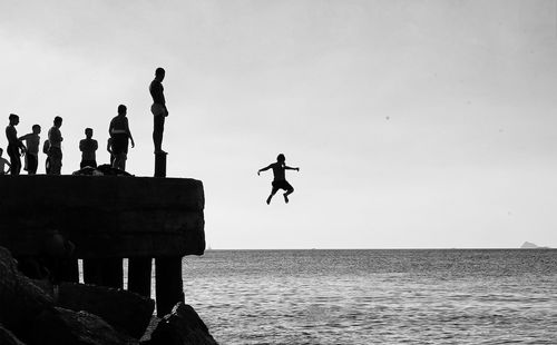 Silhouette people jumping over sea against sky