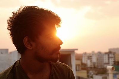 Close-up portrait of young man against cityscape during sunset