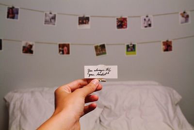 Cropped hand holding paper with text against photographs hanging against wall