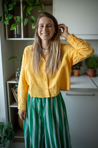 Portrait jolly happy female in yellow clothing looking at camera with cheerful smile, touching hair.