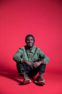 Portrait of young man sitting against red background