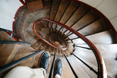 Man in stylish black boots staying on wooden spiral staircase. selective focus on male's shoes.