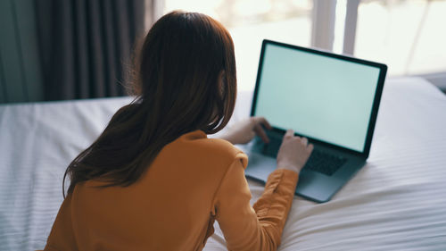 Rear view of woman using laptop at home