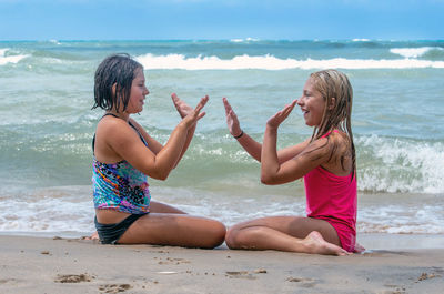 Two sister play a hand game as they sit on a sunny beach in michigan usa