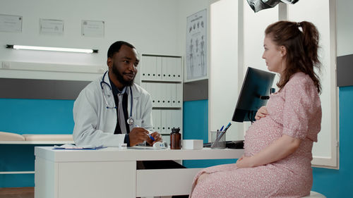 Doctor talking with pregnant woman at desk in clinic