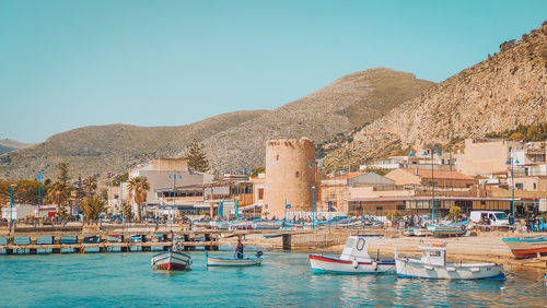 Boats in sea by buildings against clear blue sky