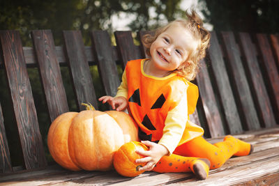 Portrait of cute girl sitting by pumpkin on swing