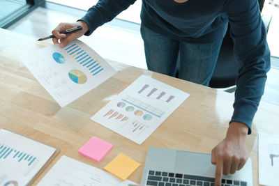 Midsection of businessman holding document while working at laptop on table in office