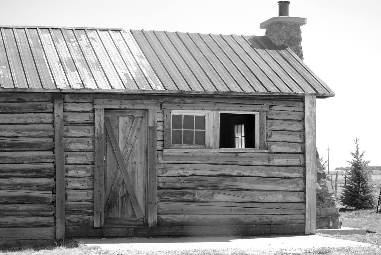 OLD WOODEN HOUSE ON FIELD BY BUILDING AGAINST SKY