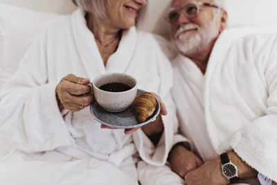 Senior man looking at woman holding coffee on bed in hotel room