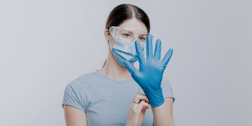 Doctor in mask wearing surgical glove against gray background