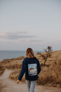 Rear view of woman standing by sea against sky