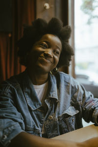 Smiling young woman wearing denim jacket while sitting at bar