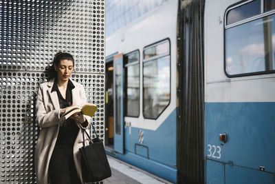 Businesswoman wearing long coat reading book while waiting at railroad station