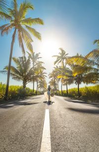 Rear view of woman walking on road against clear blue sky during sunny day