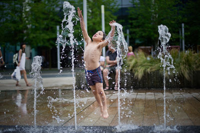 Full length of shirtless boy jumping at fountain in city