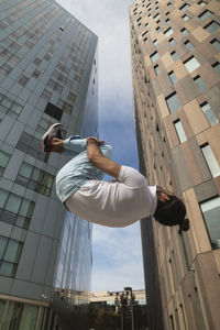 Young man practicing somersault against building in city