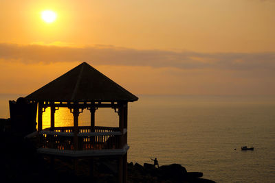 Gazebo on cliff against sea at sunset