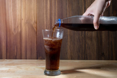 Close-up of hand pouring drink in glass on table