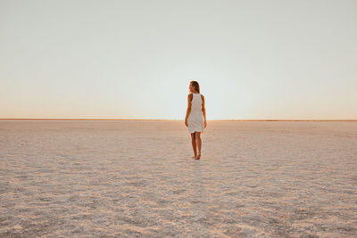 Rear view of woman standing at beach against clear sky