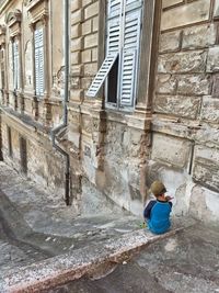 Rear view of boy sitting outside building 