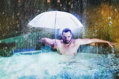 Man holding umbrella in swimming pool in the rain