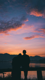 Rear view of man standing by sea against sky during sunset