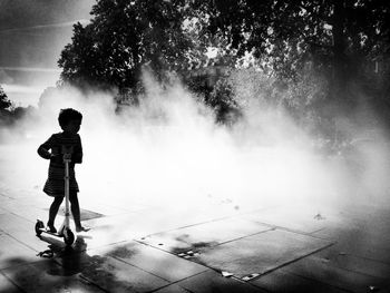 Full length of girl with push scooter amidst smoke on paving stone