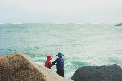 Rear view of couple fishing at shore against sky