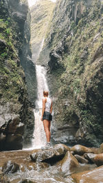 Rear view of woman standing on rock by waterfall