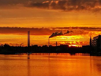 Silhouette factory against sky during sunset
