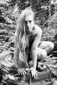 Portrait of woman crouching on lid against plants