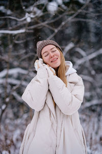 Caucasian woman in white warm jacket standing on snow. winter fashion. enjoying snow. closed eyes