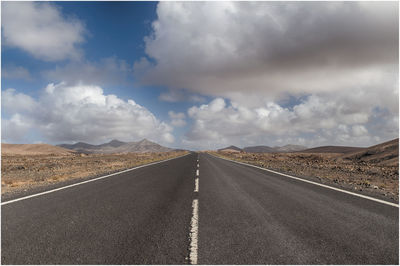 Road passing through landscape against cloudy sky