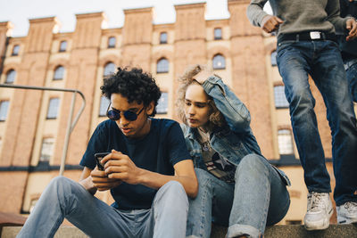 Teenage boy using mobile phone while sitting by friend in city