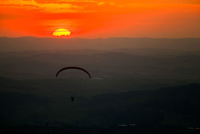 Silhouette person paragliding against mountains during sunset
