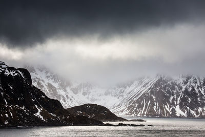 Scenic view of sea by snowcapped mountains against sky