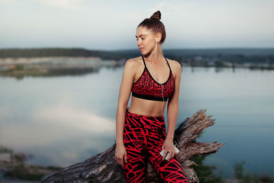 Young woman looking away while sitting by lake