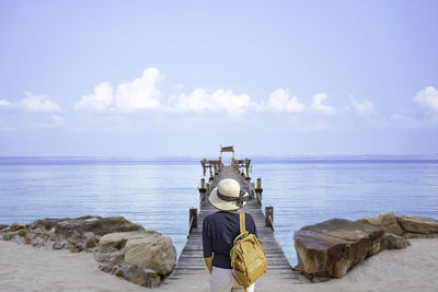 Rear view of mature woman with backpack standing on pier over sea against sky