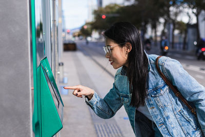 Side view of woman standing on mobile phone in city