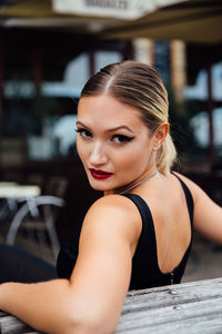 Portrait of confident young woman sitting on bench in city