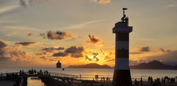 Silhouette lighthouse by sea against sky during sunset