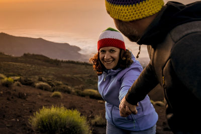 Portrait of smiling woman holding hands while standing by man on land during sunset