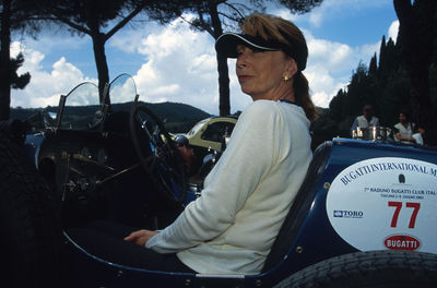 Side view of woman sitting on car against sky