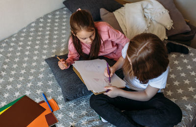 Two girls friends play at home, draw with pencils and felt-tip pens and have fun