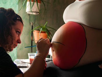 Close-up of woman painting on pregnant belly at home