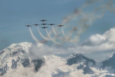 Airshow over snow covered mountains against sky