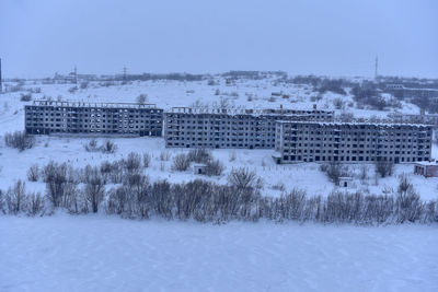 Snow covered field by buildings against sky