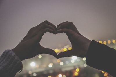 Close-up of hand holding heart shape against sky