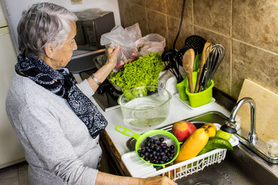 Senior woman sanding at kitchen with vegetables and fruits